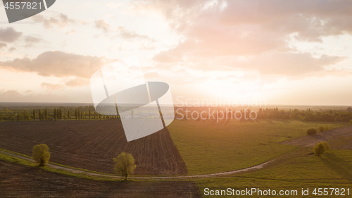 Image of Aerial view from the drone, a bird\'s eye view of abstract geometric forms of agricultural fields with a dirt road through them in the summer evening at sunset.