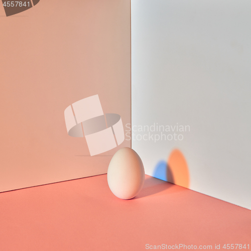 Image of Colored egg with a reflection of blue-orange shadows around a double-beige-gray background with copy space. Easter concept.