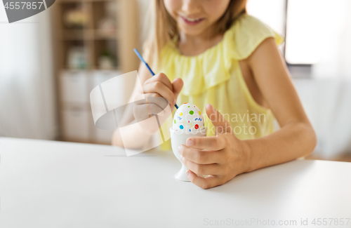 Image of close up of girl coloring easter egg by paintbrush