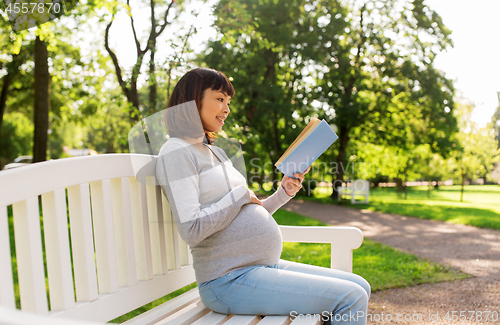 Image of happy pregnant asian woman reading book at park