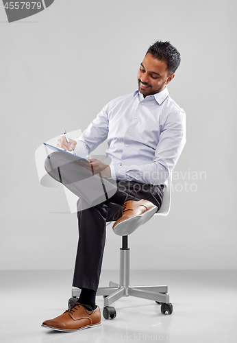 Image of smiling indian businessman writing to clipboard