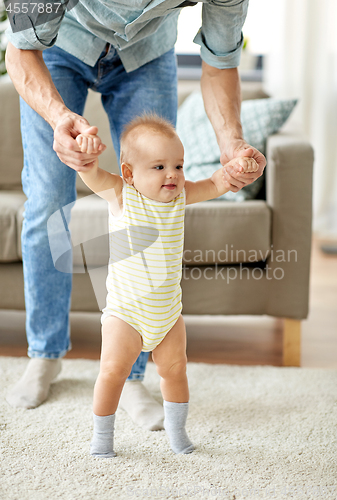 Image of father helping baby daughter with walking at home