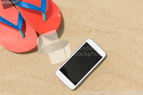 Image of smartphone and flip flops on beach sand