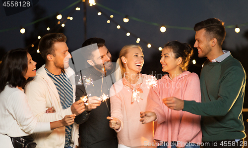 Image of happy friends with sparklers at rooftop party