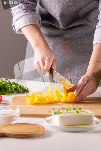 Image of Pieces of pepper on a wooden board, female hands cut vegetable for salad on a white kitchen table