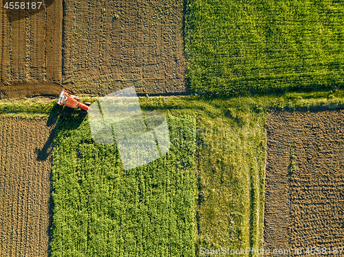 Image of Aerial view from the drone, a bird\'s eye view of agricultural fields with a road through and a tractor on it in the spring evening at sunset