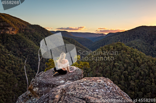 Image of Woman on a rock with views of sunset over mountain valley gorge