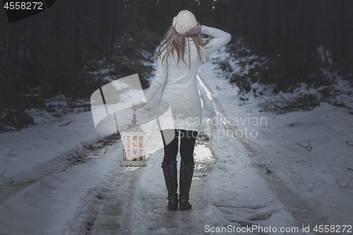Image of Woman walking along an icy road in winter with lantern
