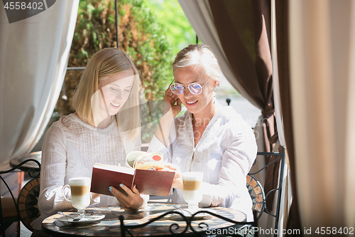 Image of Portrait of beautiful mature mother and her daughter holding cup sitting at home