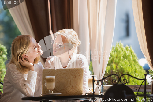 Image of Portrait of beautiful mature mother and her daughter holding cup sitting at home