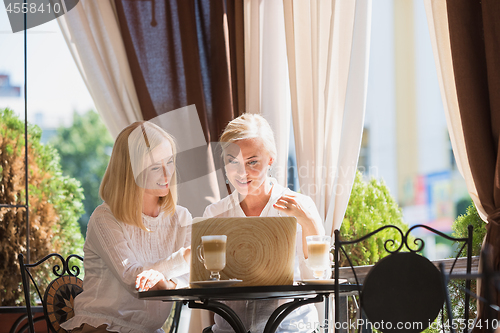 Image of Portrait of beautiful mature mother and her daughter holding cup sitting at home