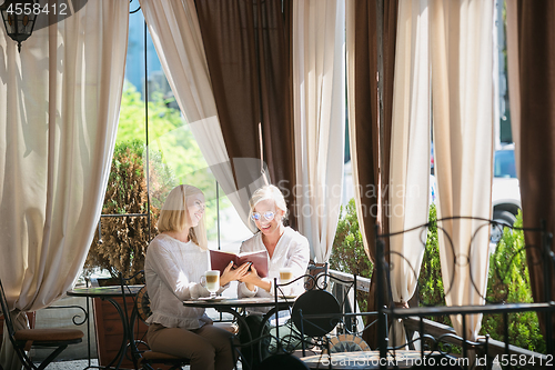 Image of Portrait of beautiful mature mother and her daughter holding cup sitting at home