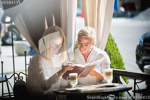 Image of Portrait of beautiful mature mother and her daughter holding cup sitting at home