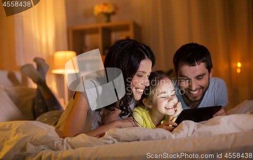 Image of family with tablet pc in bed at night at home