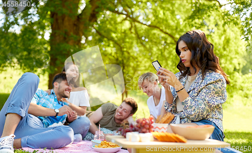 Image of woman using smartphone at picnic with friends