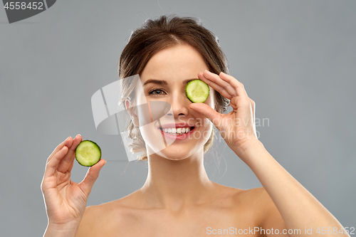 Image of smiling woman with cucumber over grey background