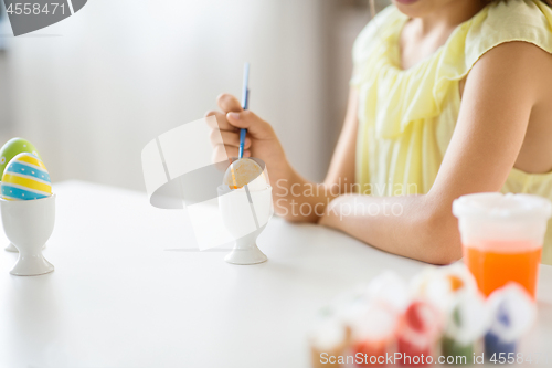 Image of close up of girl coloring easter egg by paintbrush