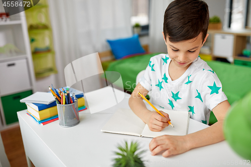 Image of happy boy writing or drawing to notebook at home