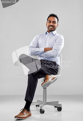 Image of smiling indian businessman sitting on office chair