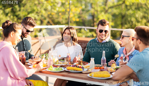 Image of happy friends eating and drinking at rooftop party