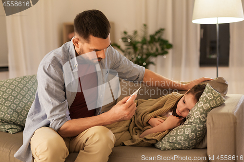 Image of father with thermometer and ill daughter at home
