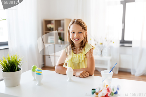 Image of happy girl with easter eggs and colors at home