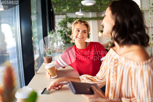 Image of female friends paying by credit card at cafe