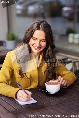 Image of happy woman with notebook drinking cocoa at cafe