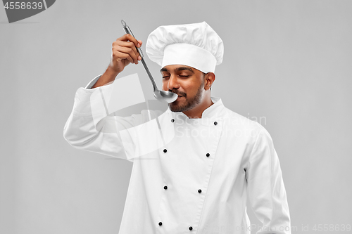 Image of happy male indian chef tasting food from ladle