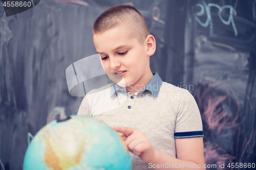 Image of boy using globe of earth in front of chalkboard