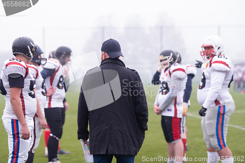 Image of american football players discussing strategy with coach