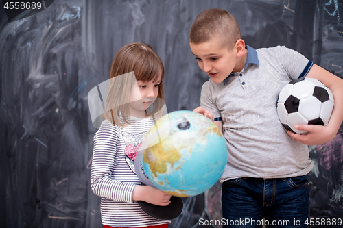 Image of boy and little girl using globe of earth in front of chalkboard