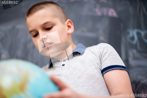 Image of boy using globe of earth in front of chalkboard