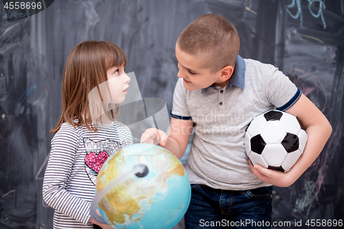 Image of boy and little girl using globe of earth in front of chalkboard