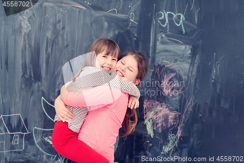 Image of little girls hugging in front of chalkboard