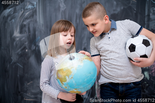 Image of boy and little girl using globe of earth in front of chalkboard