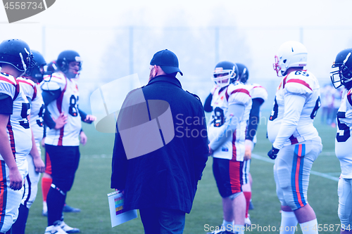 Image of american football players discussing strategy with coach