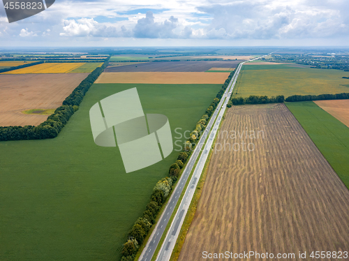 Image of Aerial view from drone of road through beautiful green field in the evening in summer.