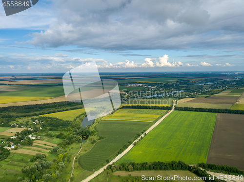 Image of Panoramic view from drone to the countryside with a country buildings, dirt road and agricultural fields against cloudy sky in the summer at sunset.