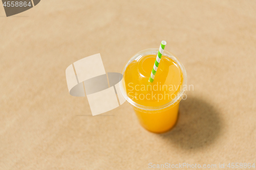 Image of cup of orange juice with straw on beach sand