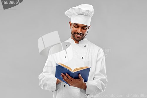 Image of happy male indian chef reading cookbook