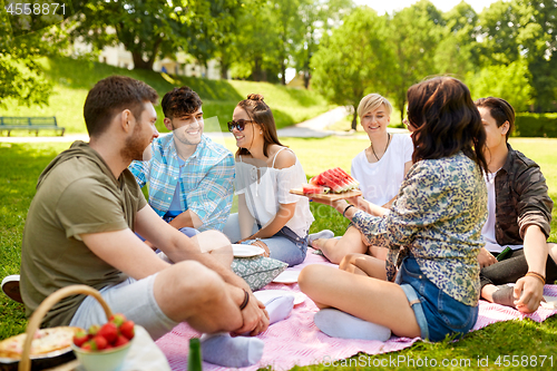 Image of happy friends eating watermelon at summer picnic