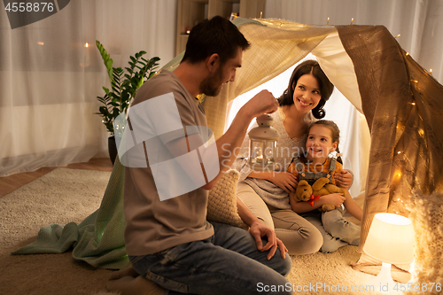 Image of happy family playing in kids tent at night at home