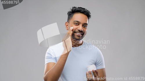 Image of happy indian man applying cream to face