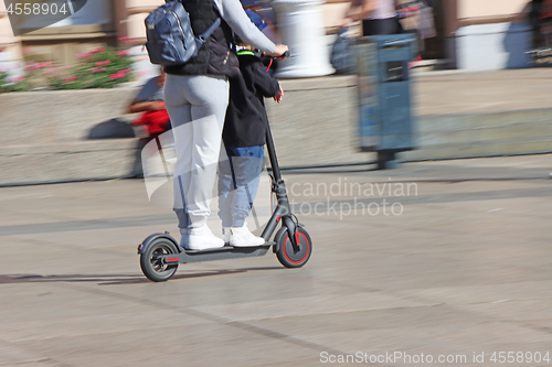 Image of Mother and son riding electric kick scooter at the city square
