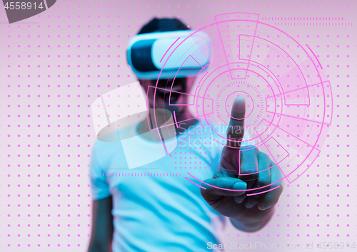 Image of Young african-american man\'s touching virtual reality in neon light