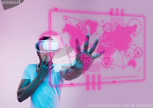 Image of Young african-american man\'s touching virtual reality in neon light