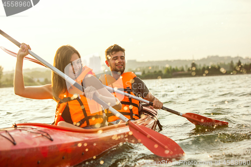 Image of Happy couple kayaking on river with sunset on the background