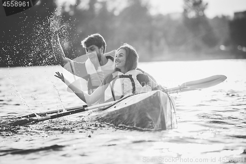 Image of Happy couple kayaking on river with sunset on the background