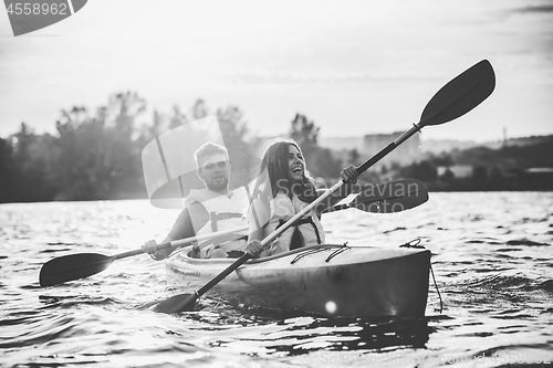 Image of Happy couple kayaking on river with sunset on the background